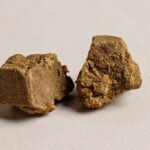 Two pieces of brown, crumbly hashish are situated against a neutral-toned backdrop.